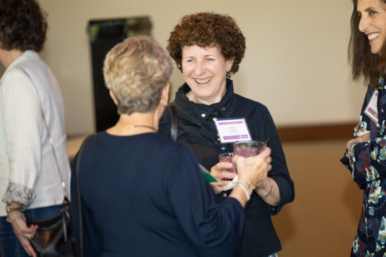 A smiling woman with a drink having a conversation with another woman