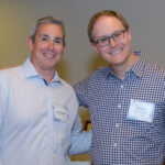 Two men in button downed shirts smiling