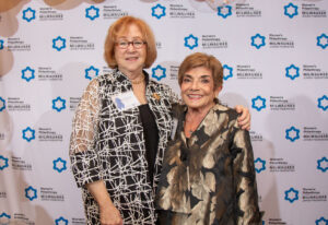 two women smiling at an event with balloons behind them