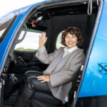 A woman waving sitting in an airplane