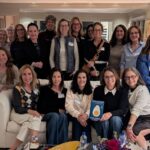 Large group of women in a living room where one person is holding a book.
