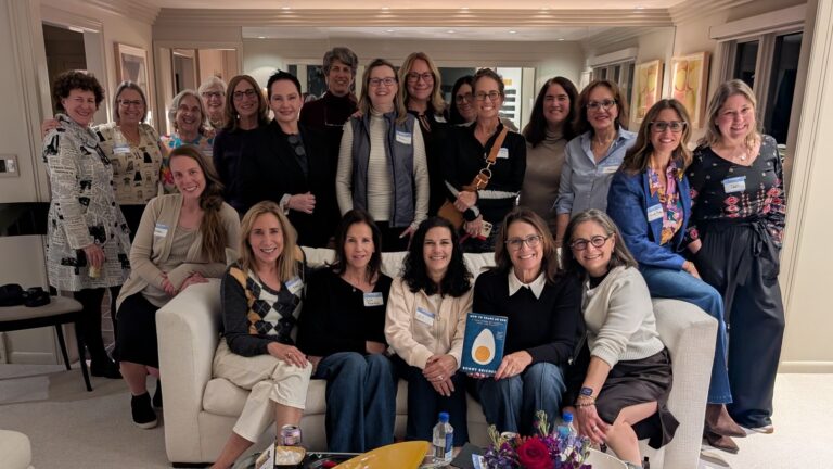 Large group of women in a living room where one person is holding a book.