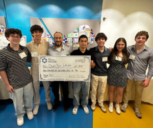 Teens posing for photo, presenting large grant check to nonprofit recipient.
