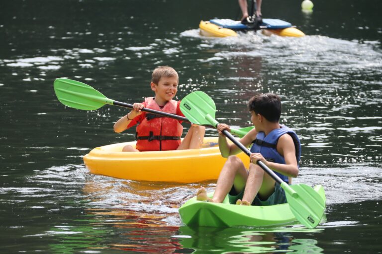 two young boys kayaking on a lake and smiling