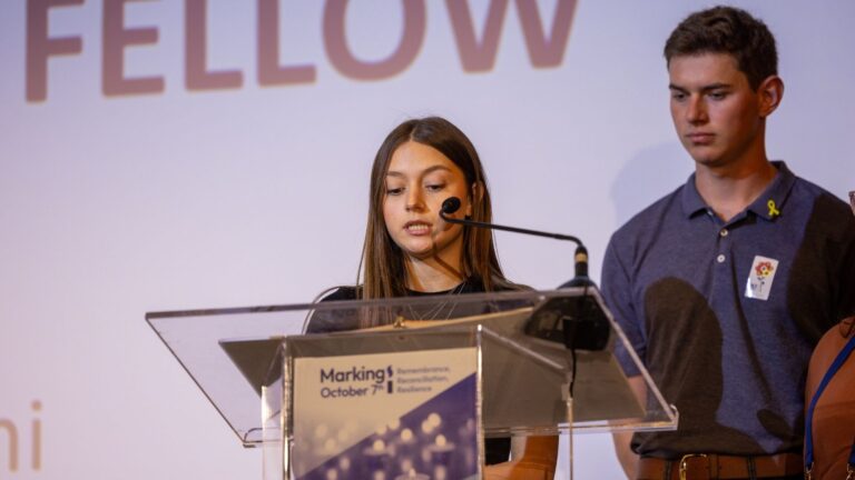 a woman speaking at a podium with man in background