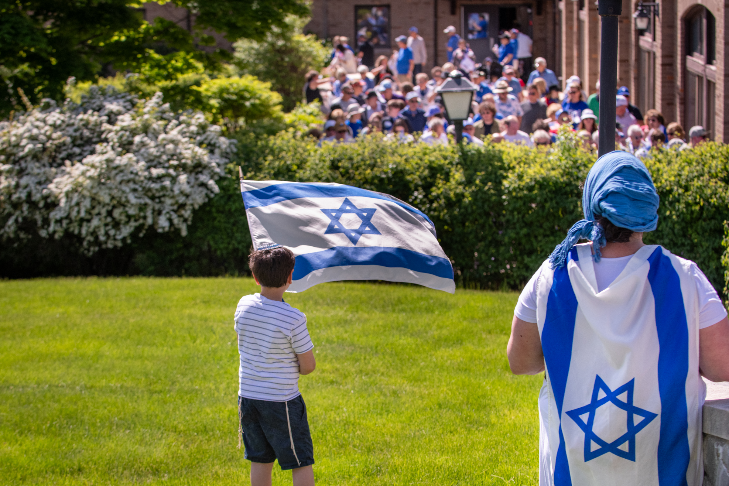 Child waving a flag while a crowd approaches in the background.