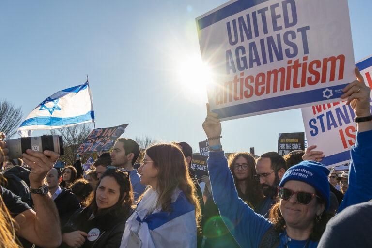 Crowd of people at a March, a Lady holding a sign up "United Against antisemitism"