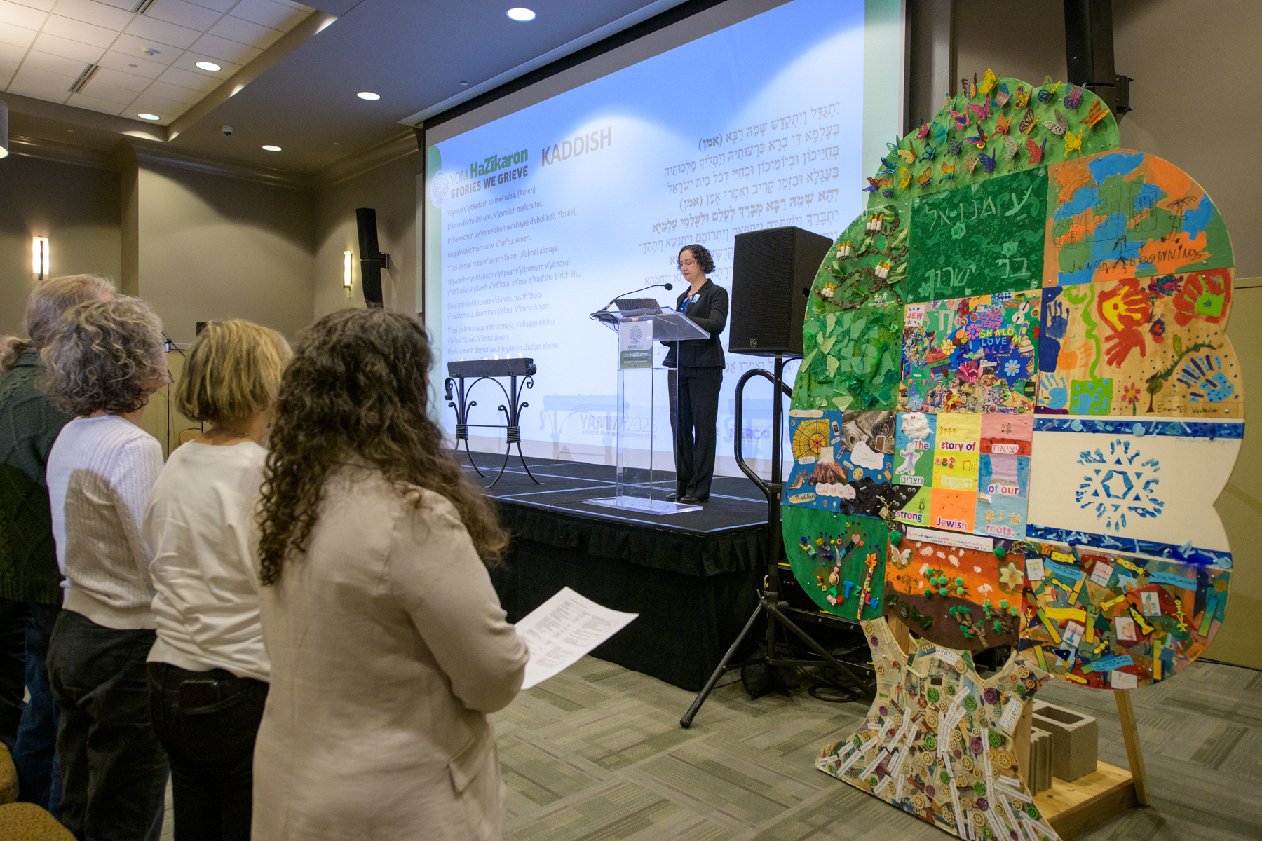 A woman speaking at podium with tree of life