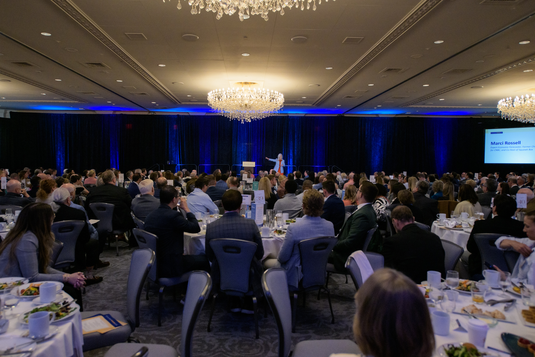 A woman giving a presentation to a large ballroom of attendees
